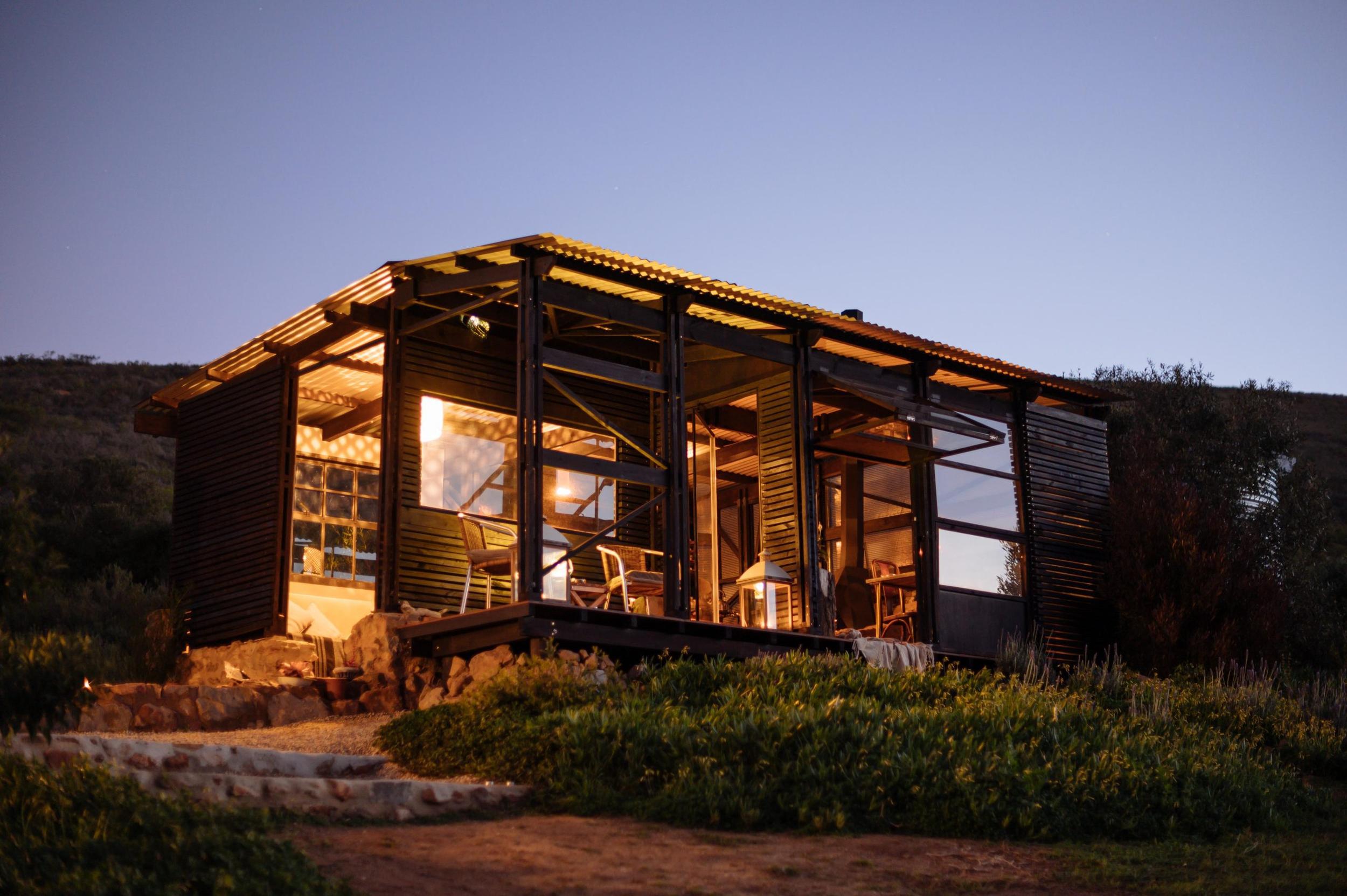 Southern Yurts: Lit cabin at dusk, warm window glow, deck chairs