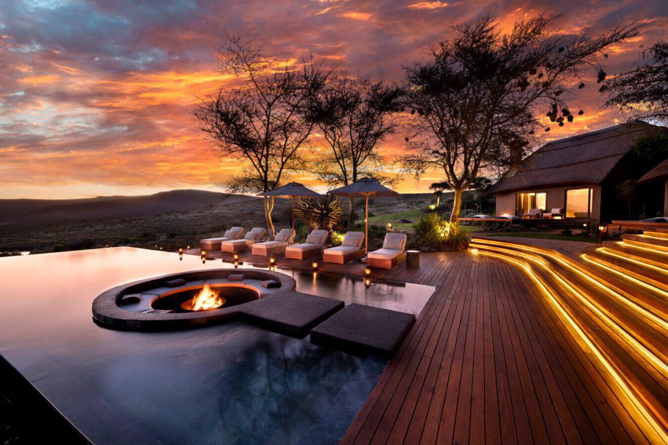 Melozhori Main Lodge: Infinity pool, fire pit, glowing deck steps at fiery sunset