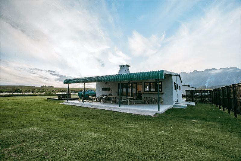 Suikerbos Cottage at Bokrivier: White cottage with covered patio, dramatic dusk sky and mountains